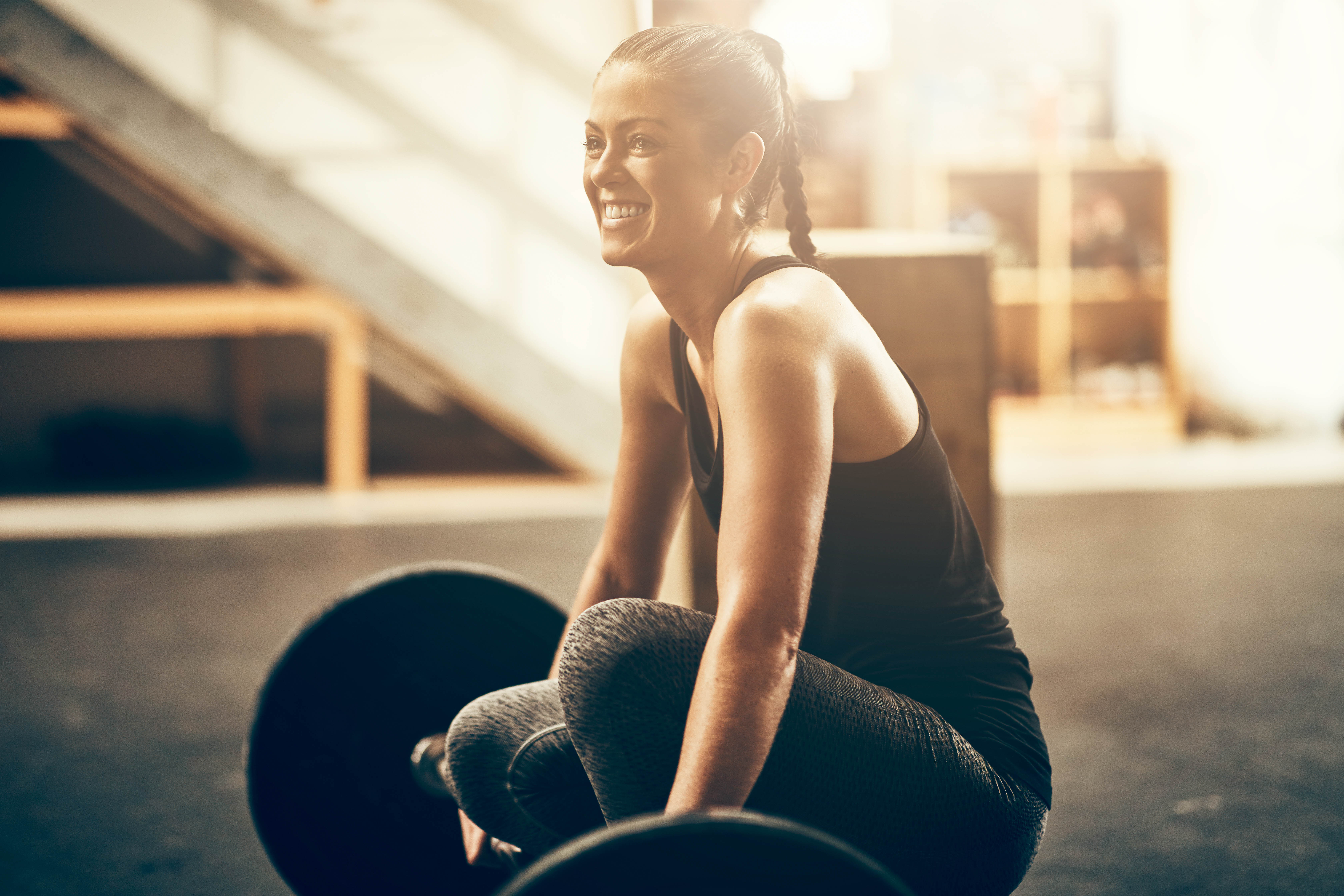 Young woman smiling as she kneels down next to her barbell in a gym